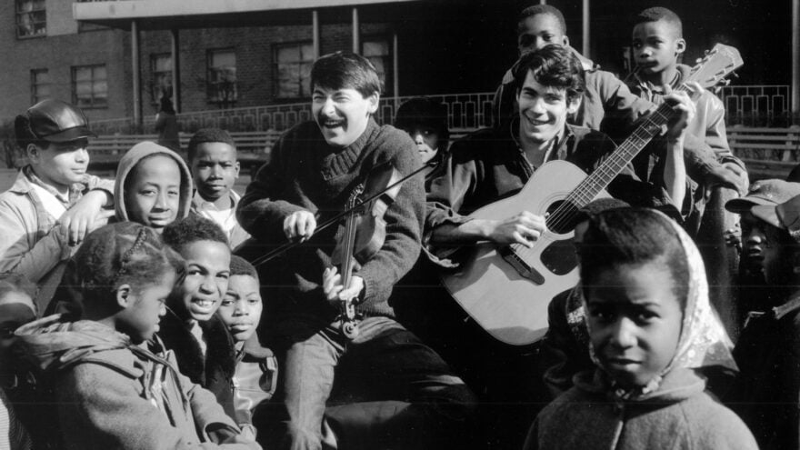 two guys with guitars surround by kids outside - black and white photo from long ago
