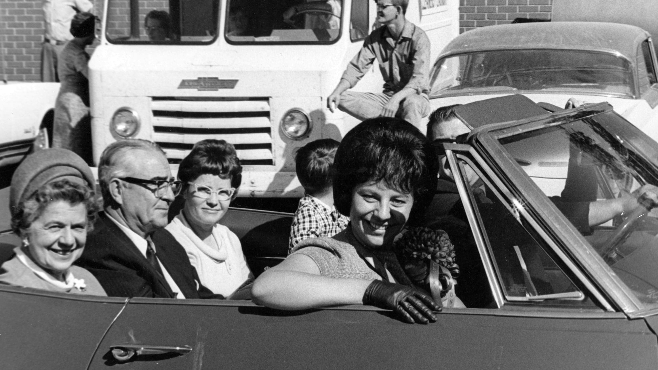 a black and white older photo of a group of people in a convertable