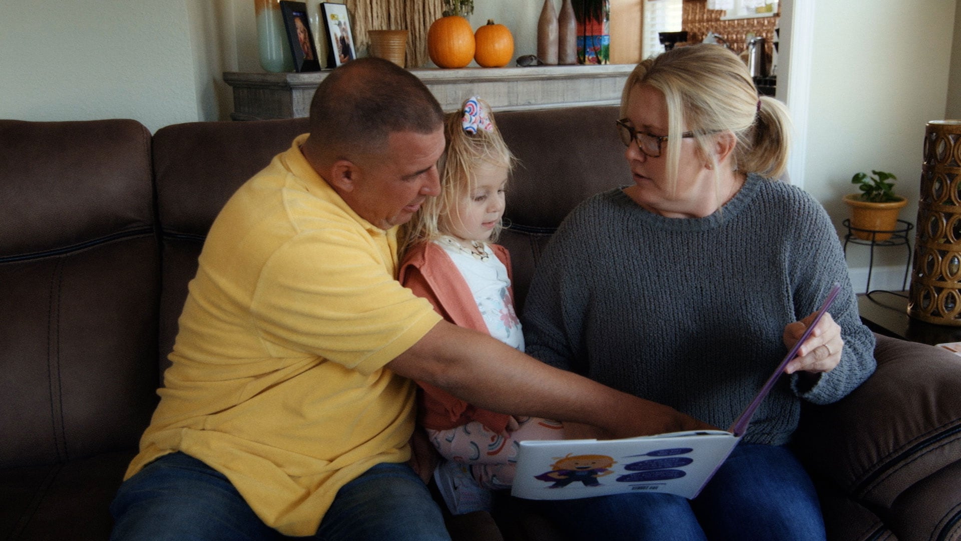 Woman and Man sitting on couch with little girl on lap looking at a picture book.